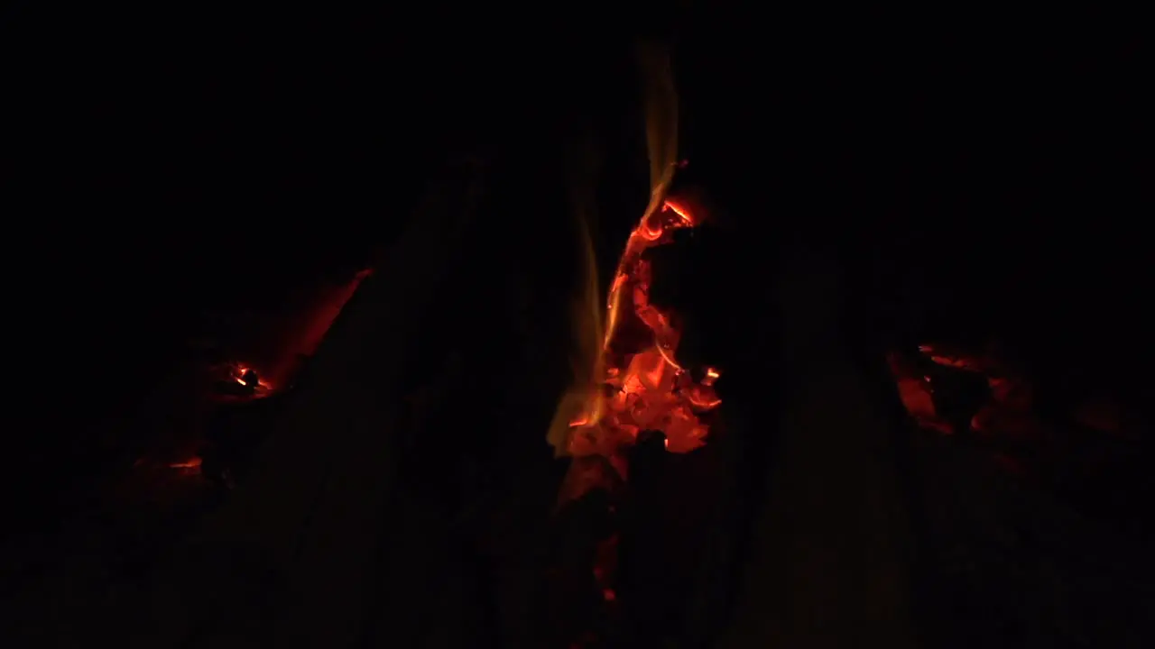 Embers of coal glowing red hot with small flames burning in wood fire filmed as close up in slow motion