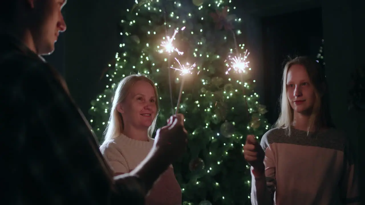 A happy family celebrates the new year at the Christmas tree holding burning sparklers