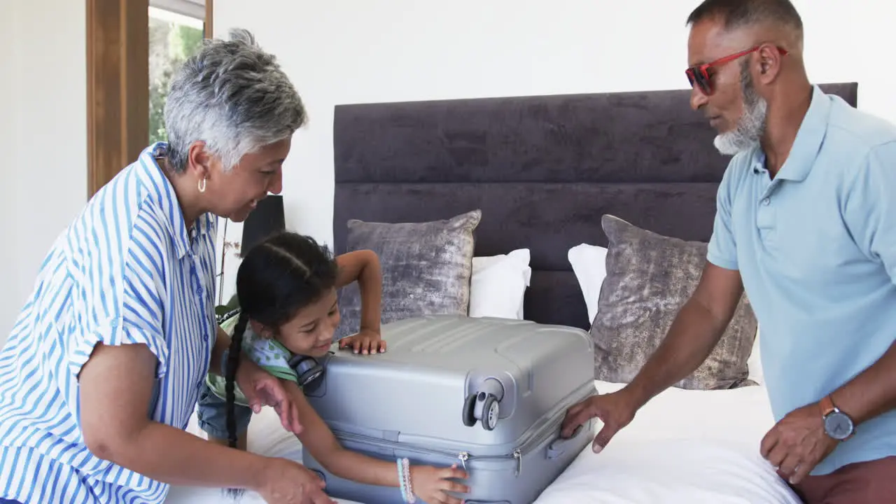 Biracial grandparents with their granddaughter unpack a suitcase on a bed