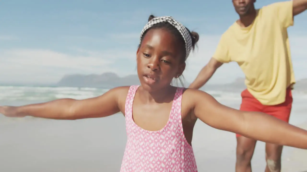 African american father and daughter with arms wide open enjoying at the beach