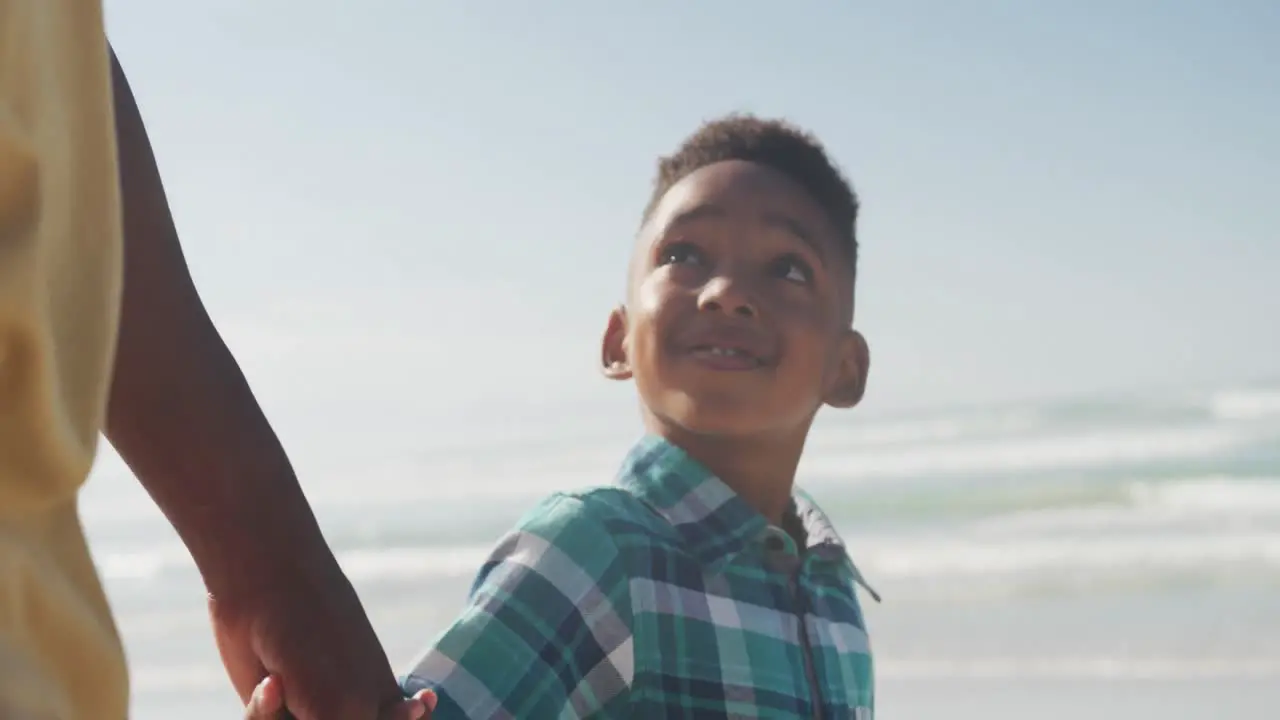 African american son holding his father's hand while walking on the beach