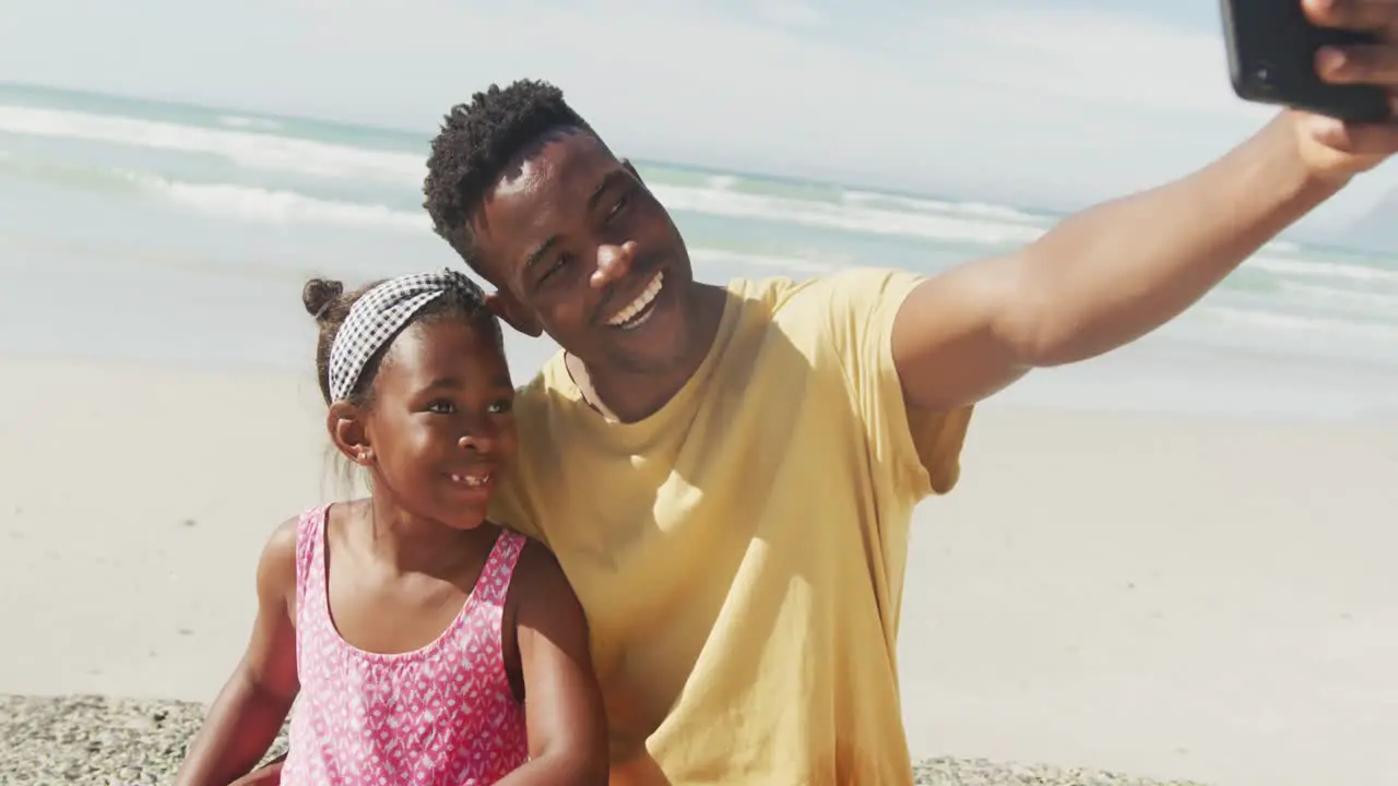 African american father and daughter talking a selfie at the beach