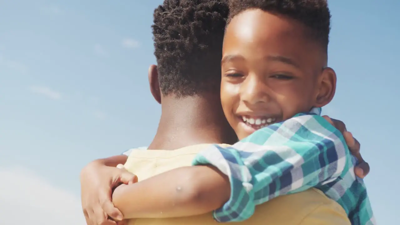 African american son smiling while hugging his father at the beach