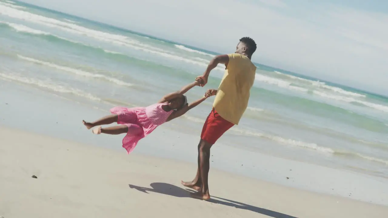 Playful african american father spinning his daughter on the beach