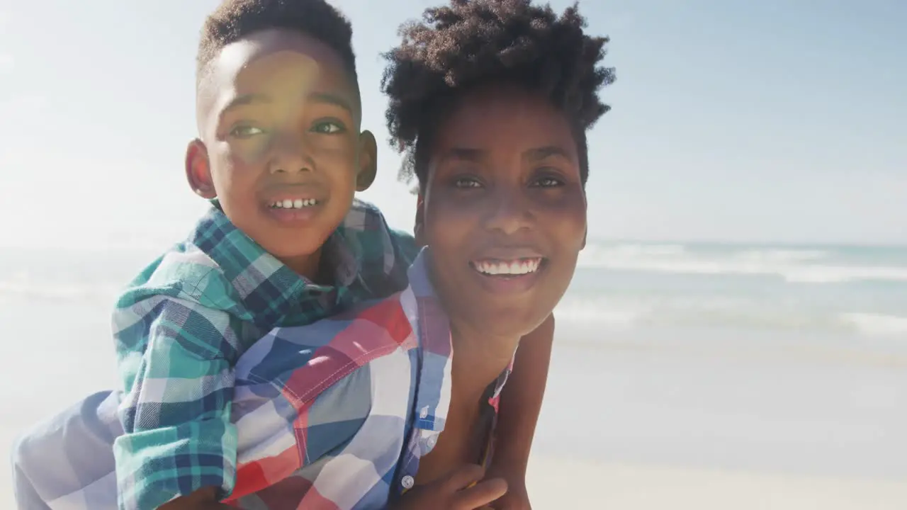 African american mother giving piggyback ride to her son at the beach