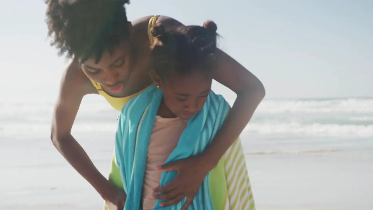 African american mother drying her daughter with a towel at the beach