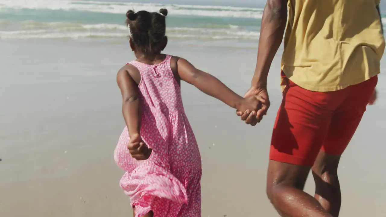 African american father and daughter holding hands running on the beach