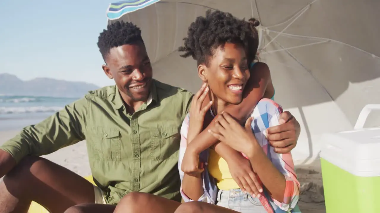 African american family smiling while sitting under a umbrella on the beach