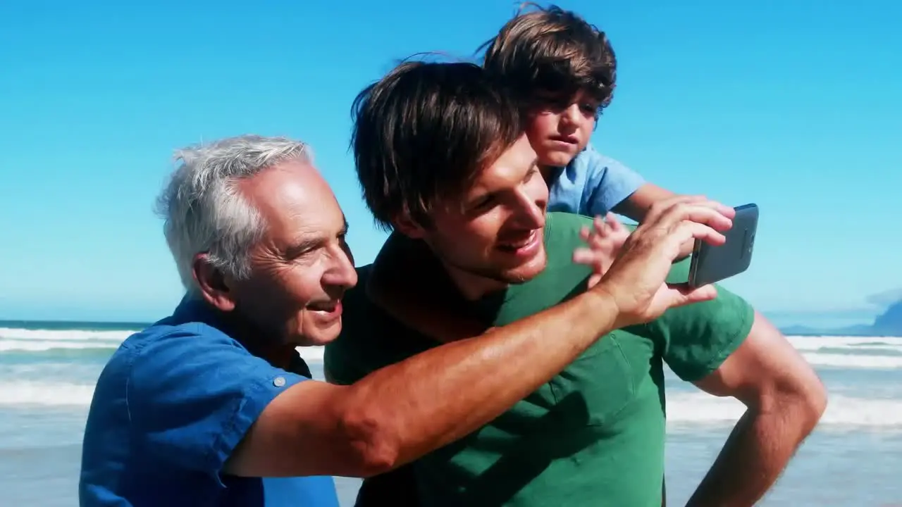 Abstract shapes over vibes text against grandfather father and son having a video call at beach