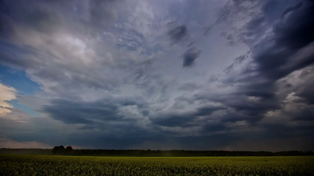 Dark stormy clouds flow in over an endless farmland field of rapeseed cloudscape time lapse