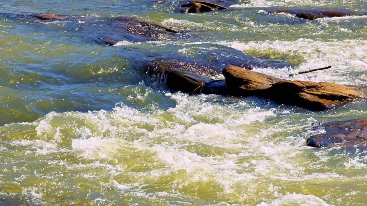 Foamy white water river rapids flowing over rocks in bright sunlight