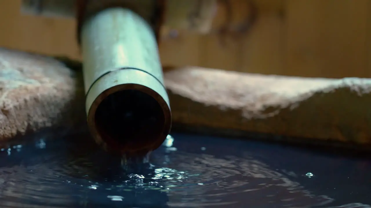 Natural hot spring water flows from bamboo pipe into stone bath at onsen