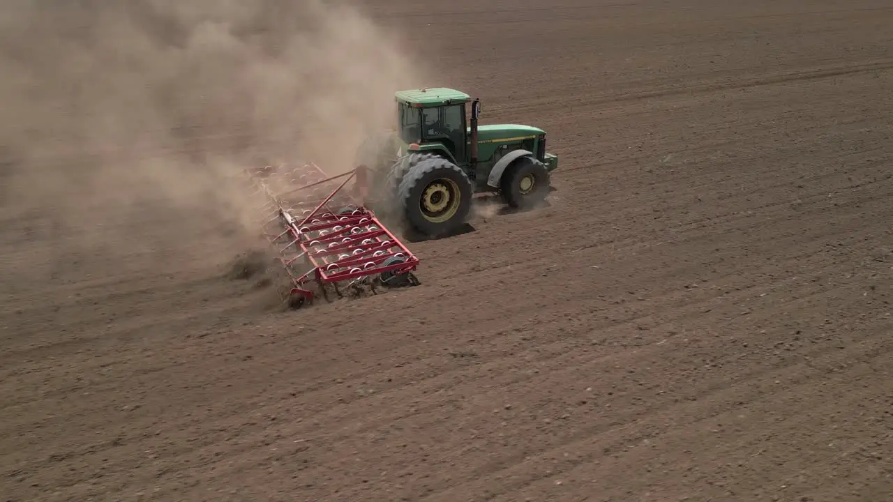 Tractor in field pulls harrow to loosen topsoil for planting crops