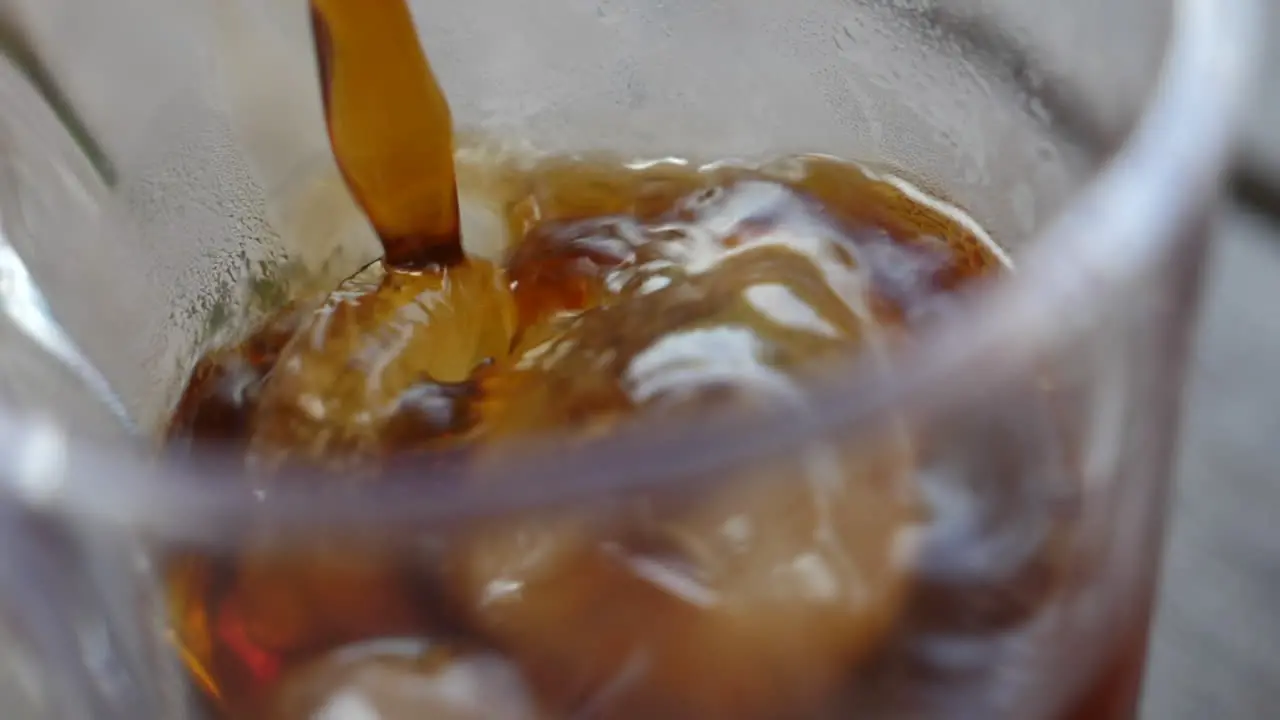 Macro slow motion of colored soda being poured into a glass with ice