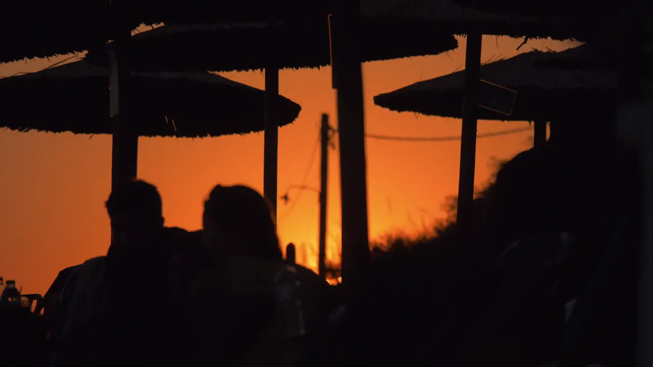 People relaxing on beach at sunset Black silhouettes on orange sky background