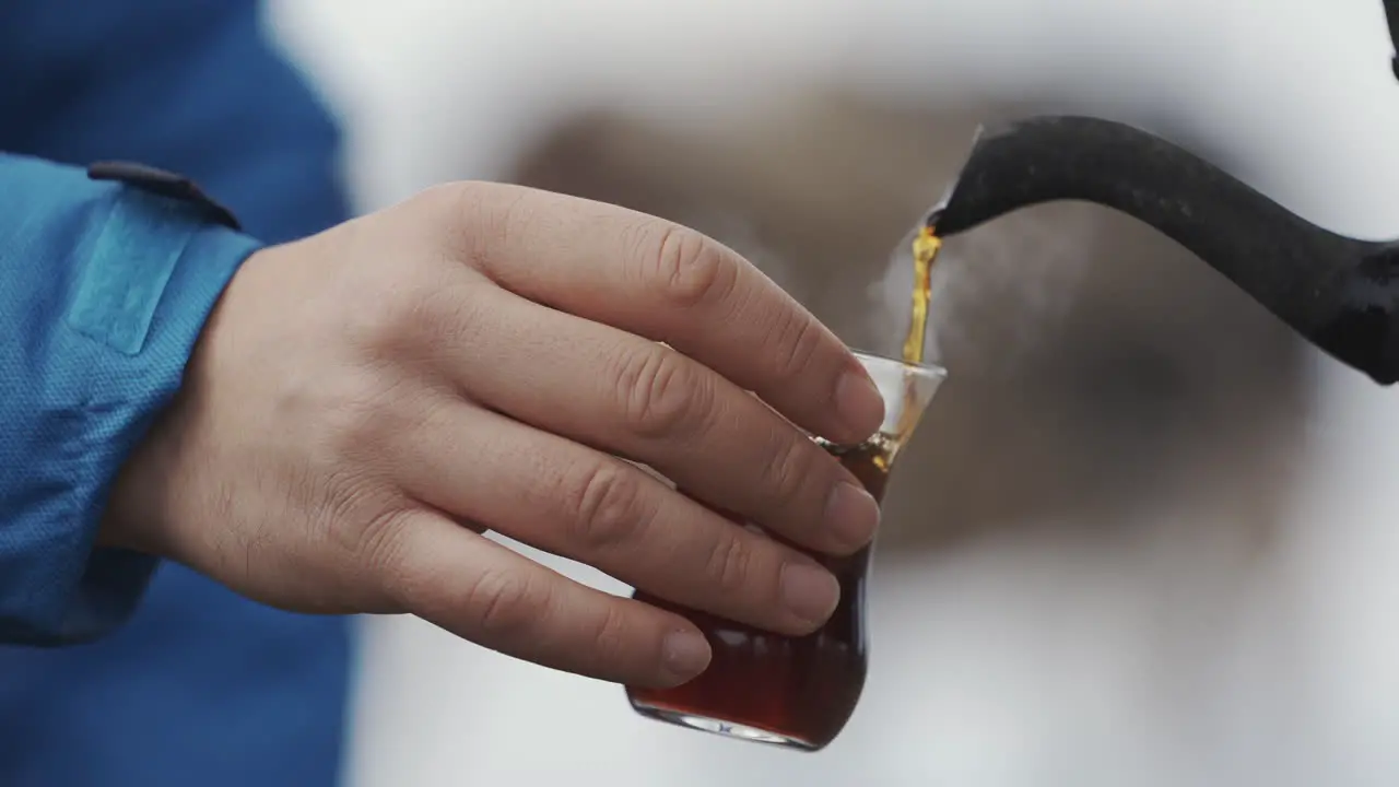 Cropped view of pouring tea into glass cup outdoors