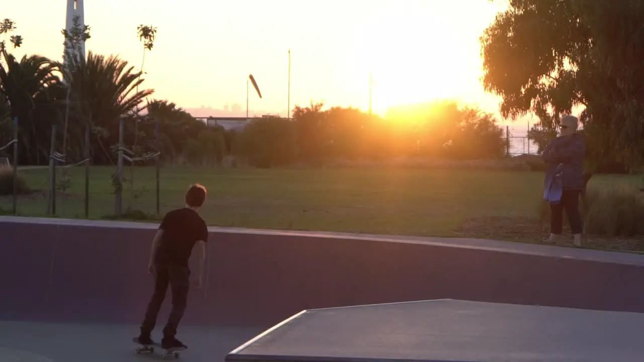 Slow motion shot of boy dropping in at a skate park skateboarding during sunset