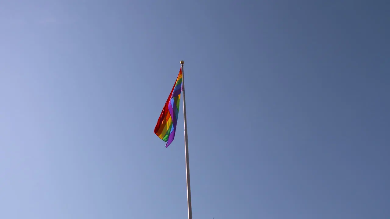 Rainbow Pride flag gently swaying against a blue sky background