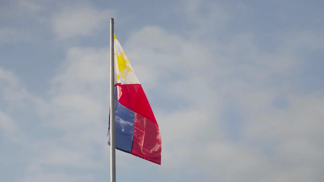 Philippine flag fluttering in the wind on a flagpole against a slightly cloudy blue sky