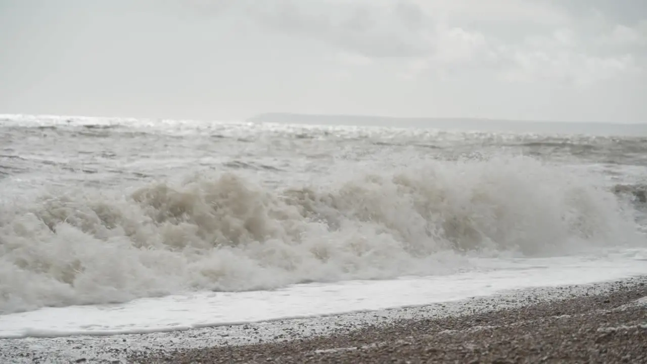 Sea waves crashing onto pebble beach on a cloudy day in Hastings England