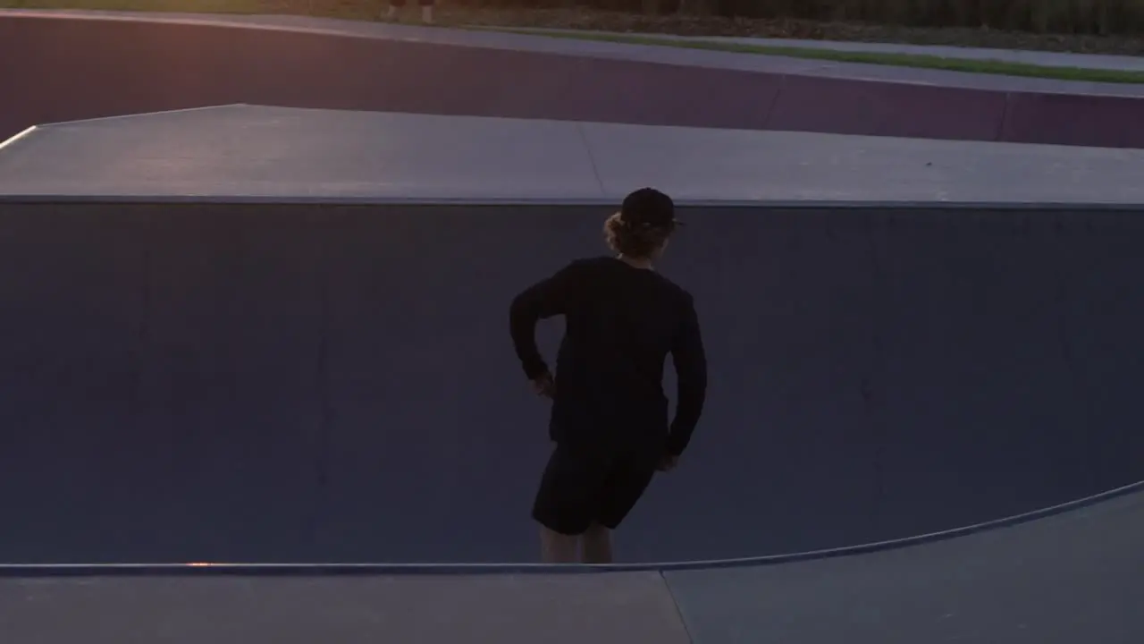 Slow motion shot of man grinding a rail at a skate park skateboarding during sunset