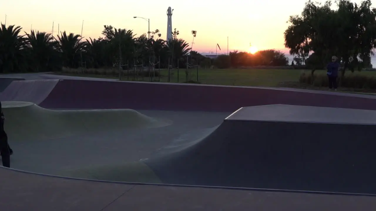 Slow motion shot of boy grinding on rail at a skate park skateboarding during sunset