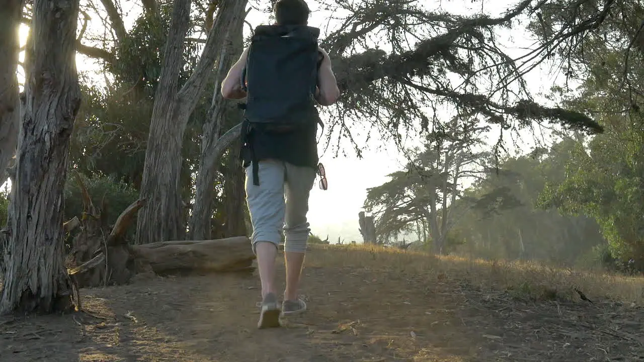 Young man traveler wearing a large black backpack walking in slow motion along the ocean bluffs during a golden sunset in Santa Barbara California