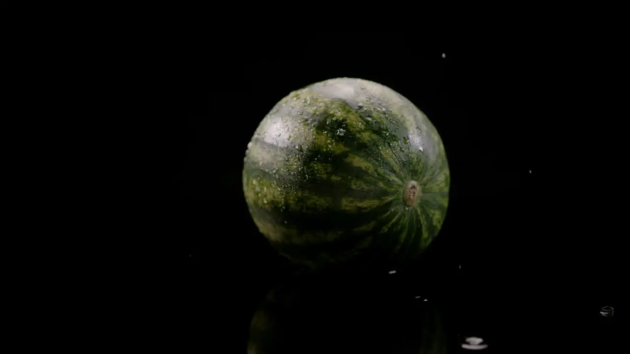 Water drops falling on watermelon isolated on black background slow motion