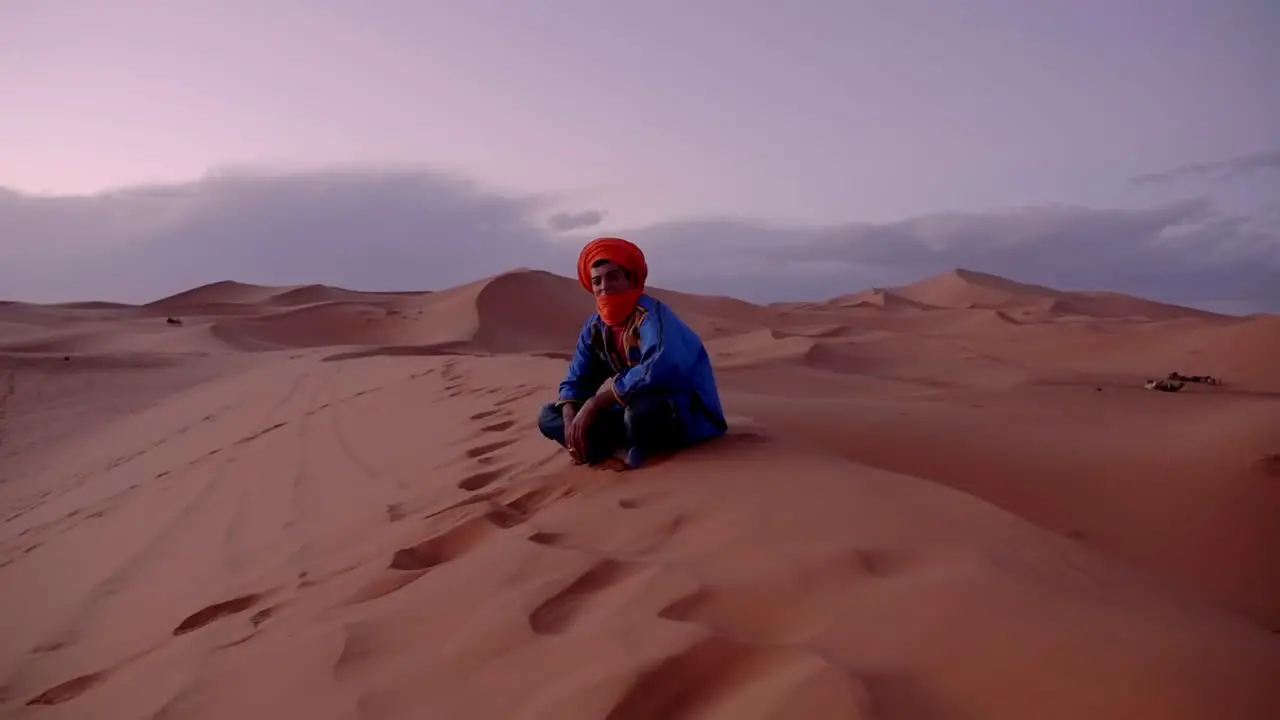 Dynamic camera movement establishing shot proud Berber moroccan man sitting on sand dunes in Erg Chubby Merzouga Morocco