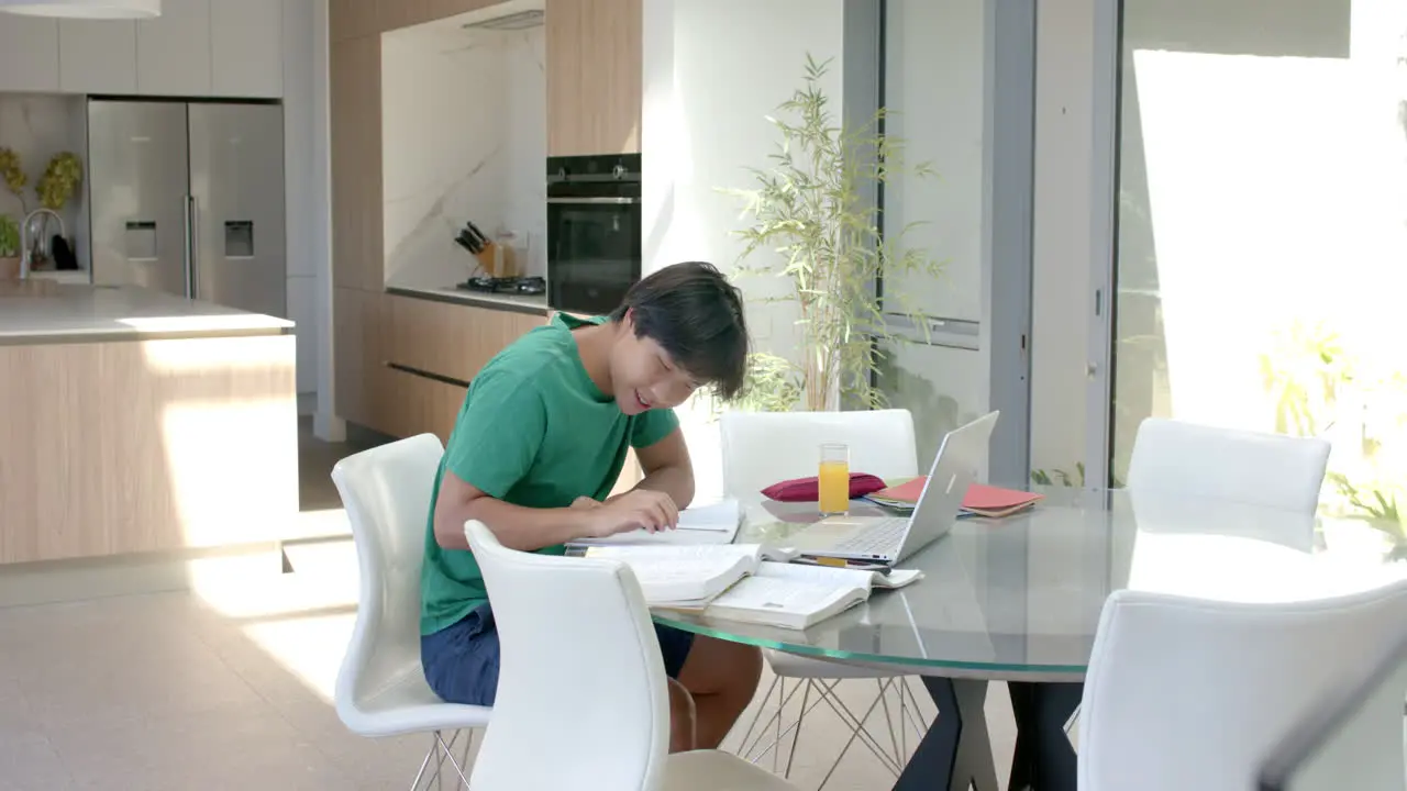 Teenage Asian boy studying on a laptop at a modern home kitchen table