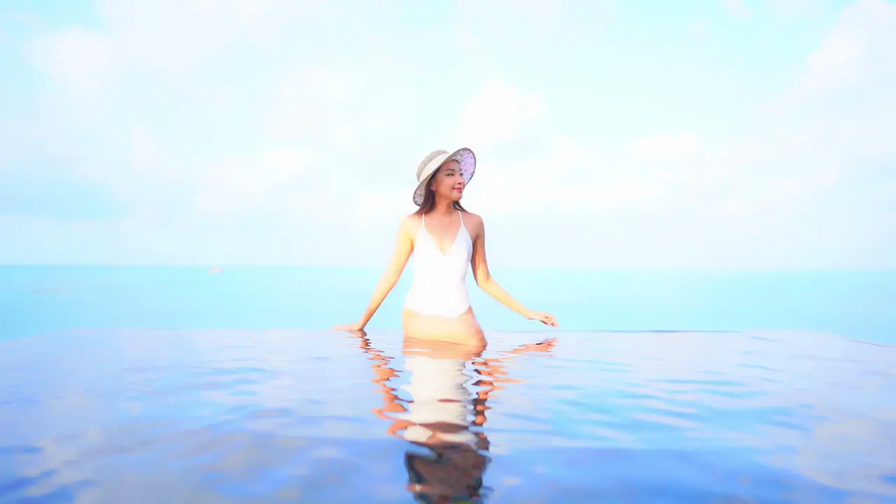 Sitting on the edge of an infinity pool makes this young and attractive woman look as if she is floating on top of the water