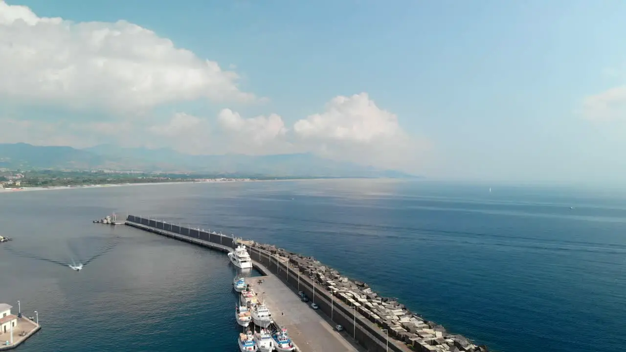 Aerial large stone ocean breakwater with boats moored on inside wide shot