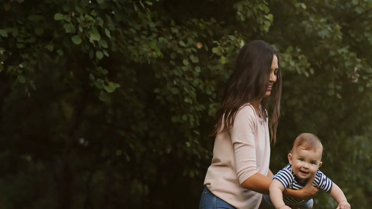 Happy Young Mother Holding Her Cute Baby In Arm Swinging As Airplane Outdoors 1