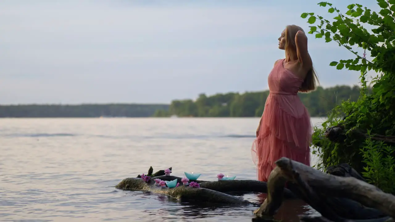 A gorgeous blonde woman wearing a pink dress in the water next to candles and flowers