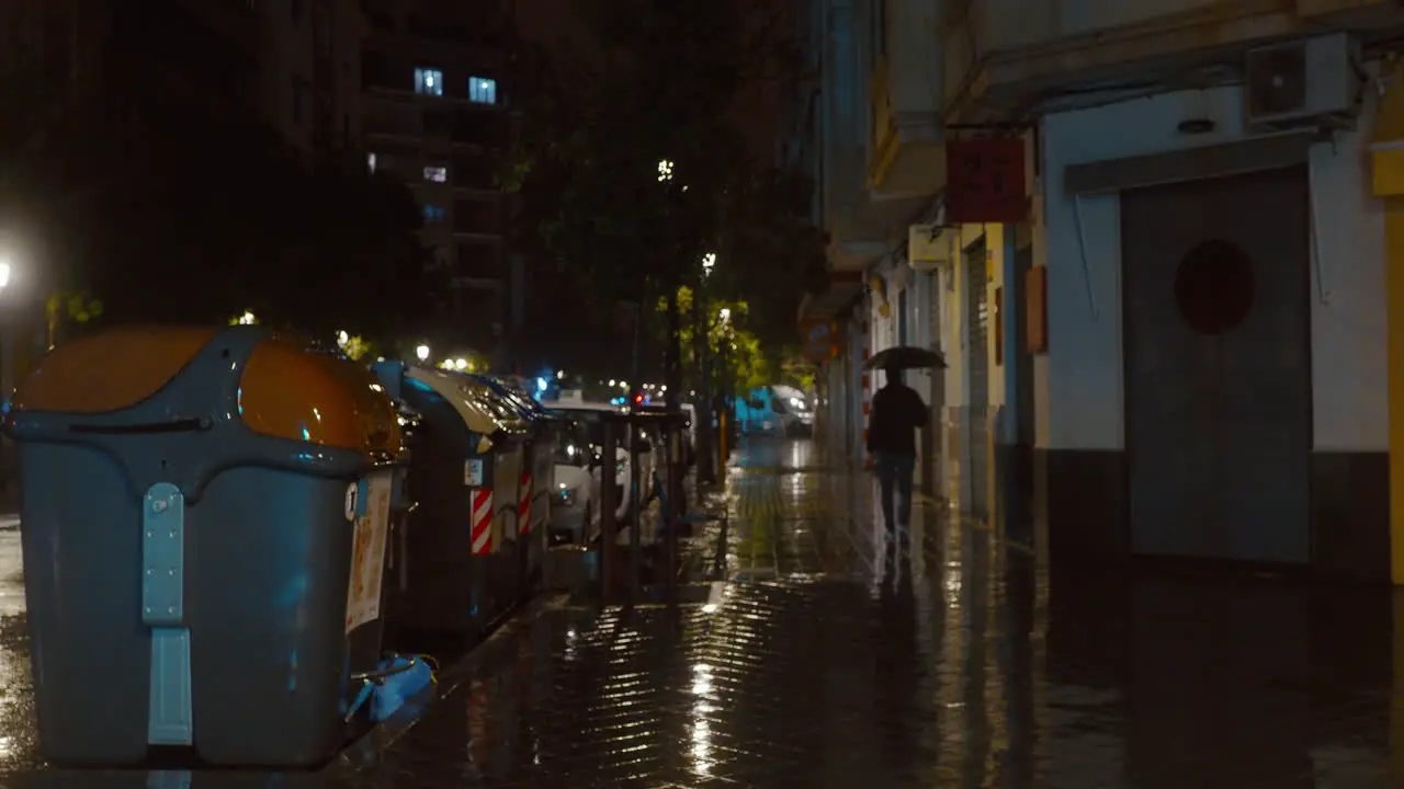 Man with umbrella walking under drizzling rain in night city