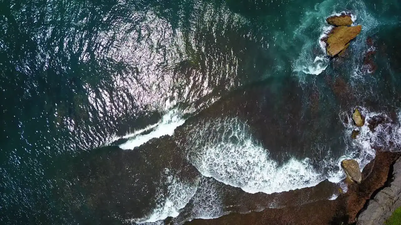 Top view of Indian Ocean waves breaking over coral rock reef with sun reflection