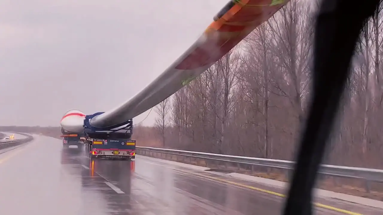 POV of a car driving on the highway on a rainy day with huge windmill fan passing on the truck