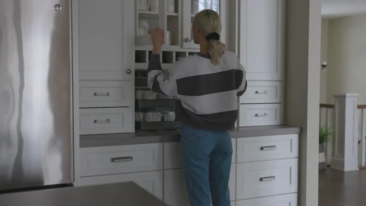 Woman walking to the cabinet to grab a mug to make a cup of coffee