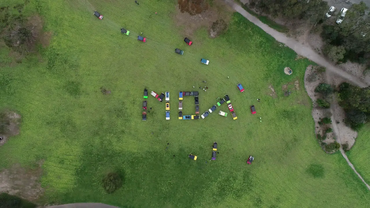 Moke Owners Association 50th Anniversary Convoy Mokes filing in one at a time in perfect unison into large word sign on green grass