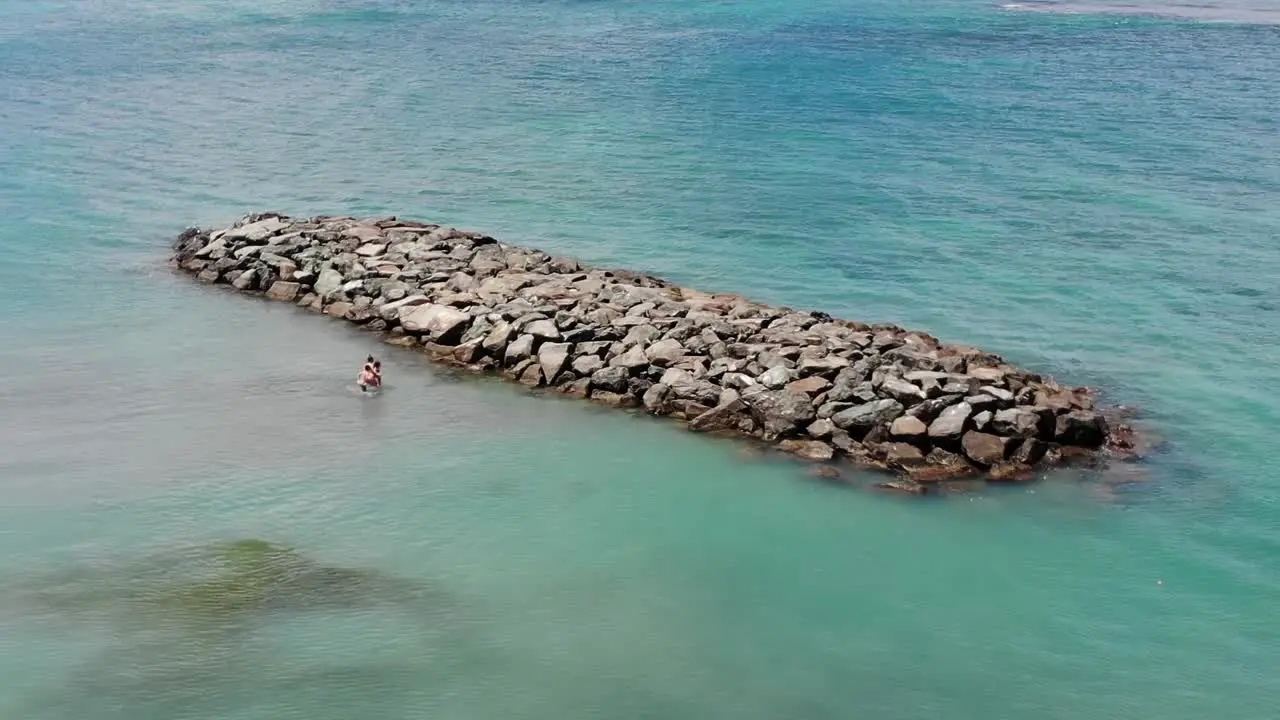 Aerial footage of a family playing in the beach by a rock formation