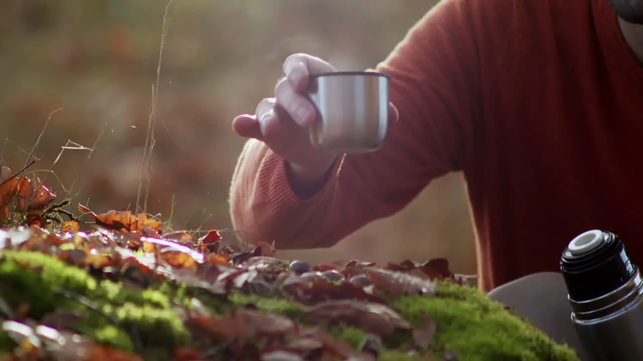 Tourist man drinking hot tea or coffee in forest close up view of hand holding thermos mug