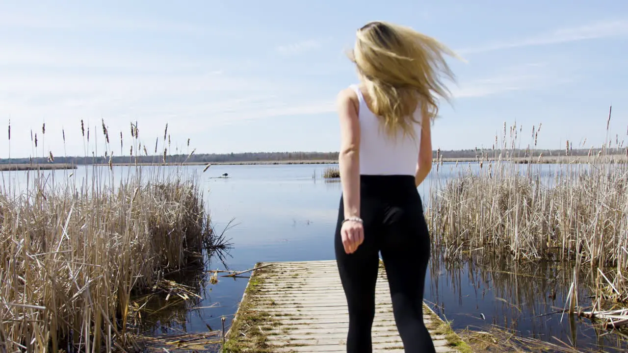 Fun confident young woman runs out on to a dock on a beautiful calm lake