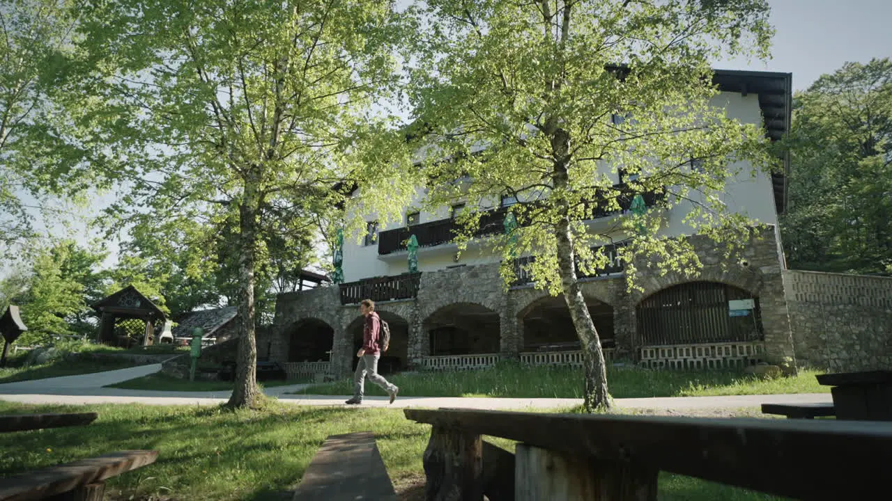 A young hiker is passing a mountain cottage past hte trees