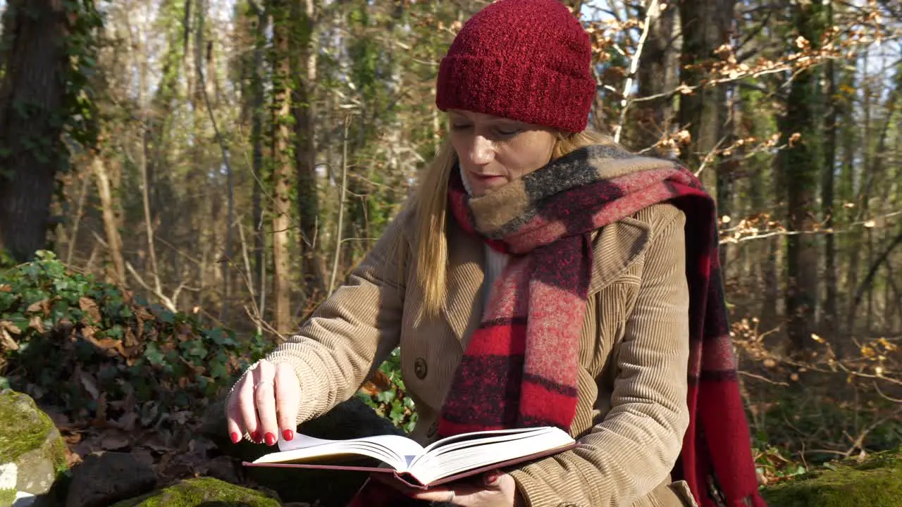 Woman reading book in forest wearing winter scarf and hat Mid Shot Orbit