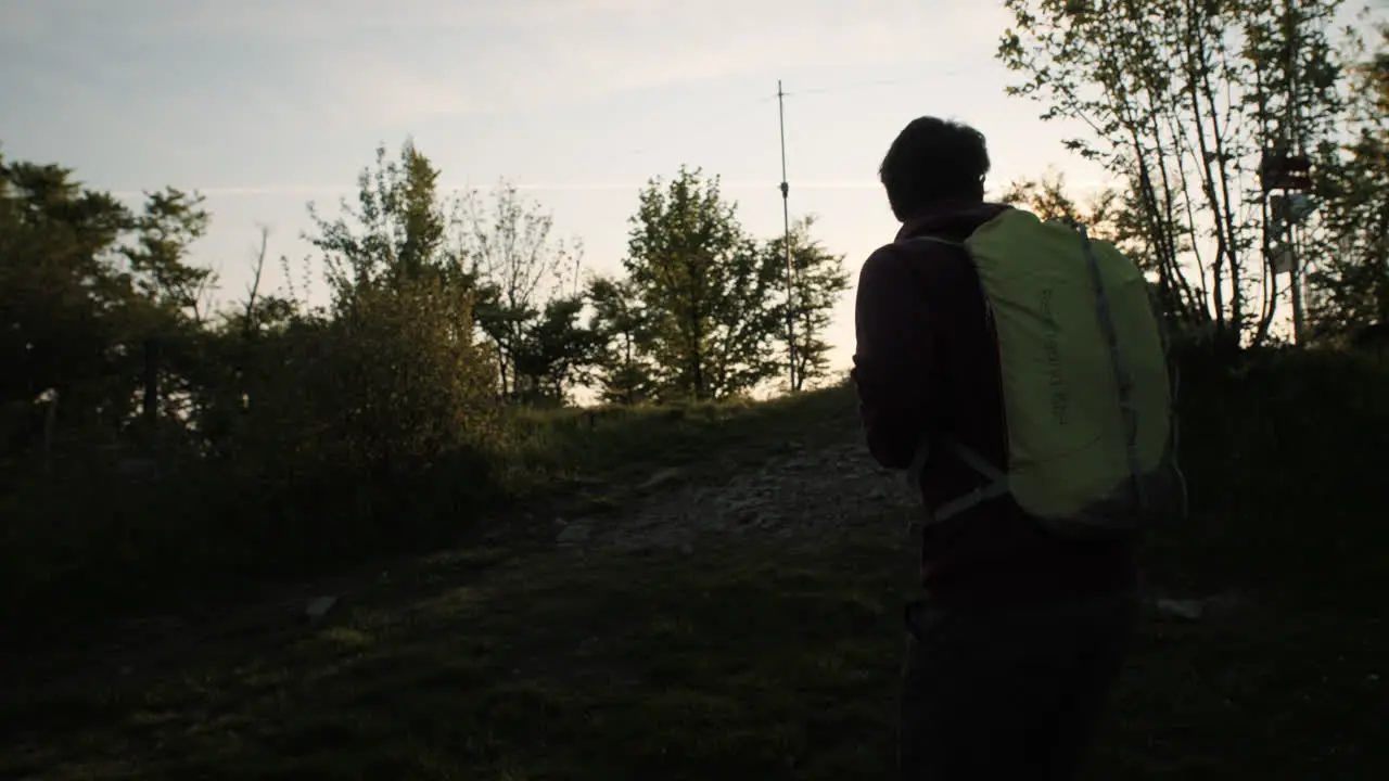 Hiker with a green backpack walks up a hill towards the sun camera tracking from behind