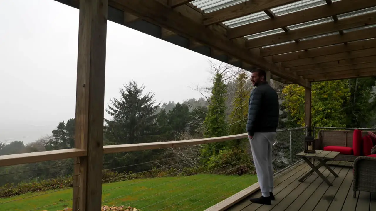 Static view man with beard looks at ocean from garden terrace on deck on rainy cloudy day