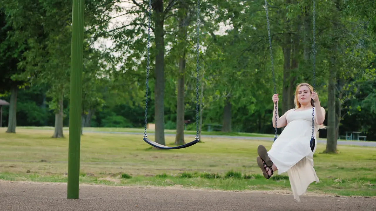 Young Pregnant Woman Riding A Swing In The Park