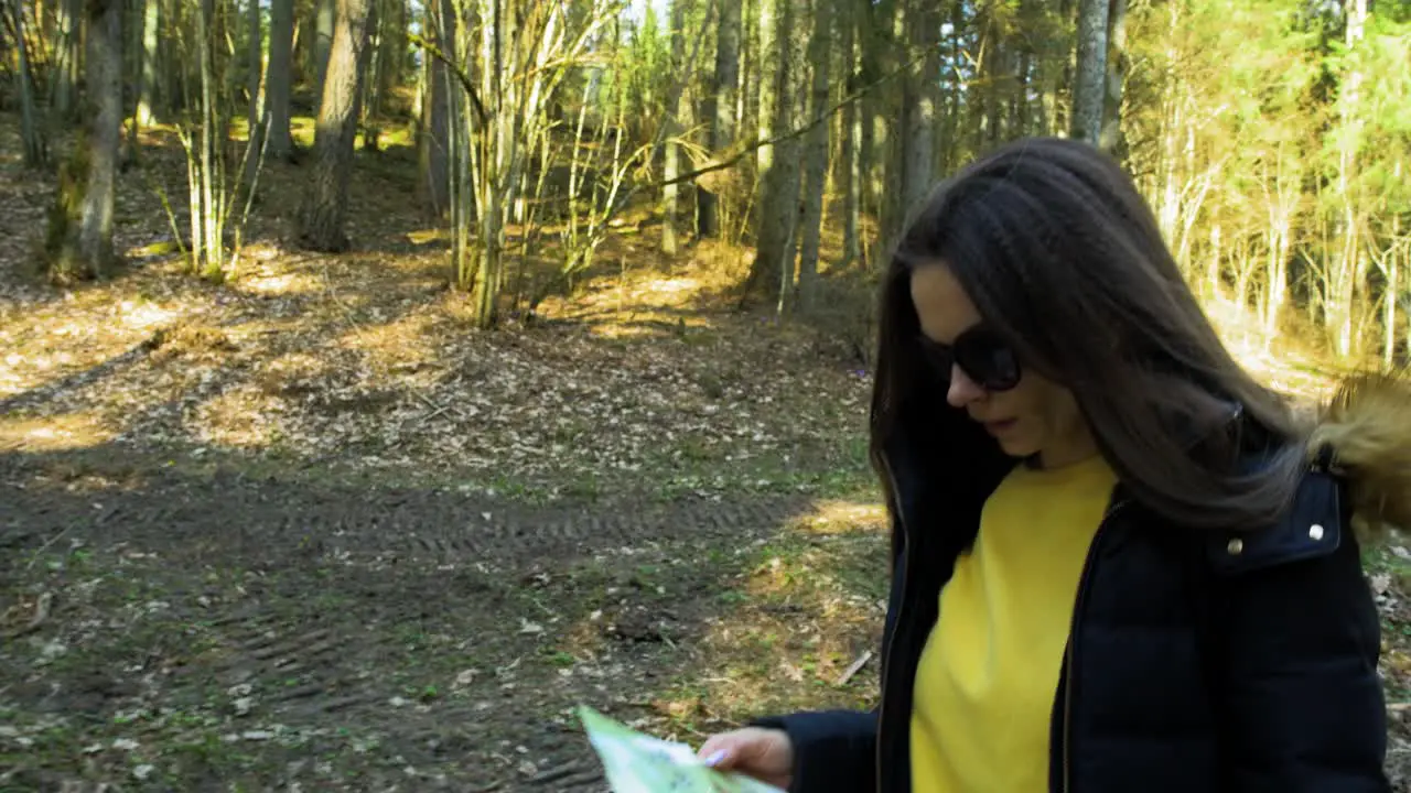 Young caucasian woman with brown hair and dark sunglasses walking in the wood map in hand beautiful sunny spring day tracking jib shot from ground up