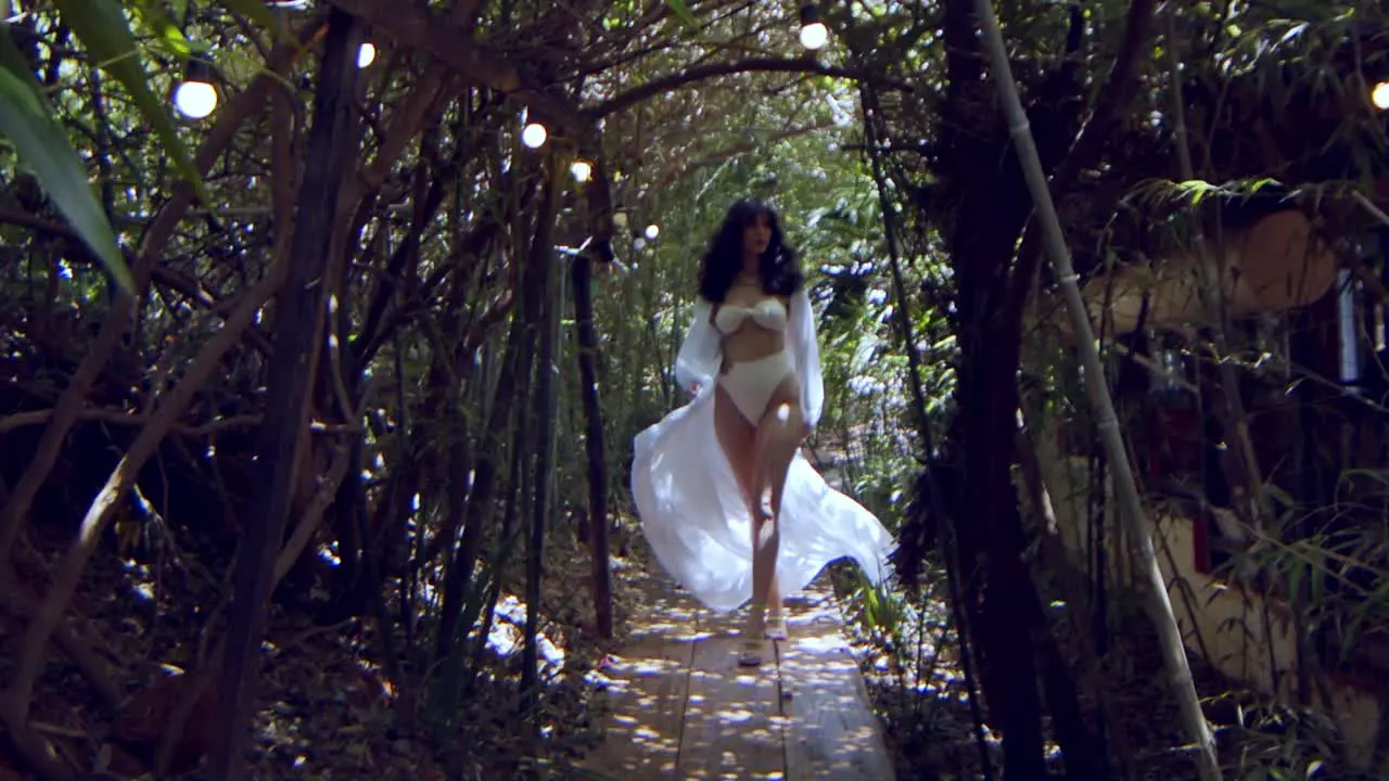 Gorgeous model in a white bikini and white dress walks through a jungle in slow motion