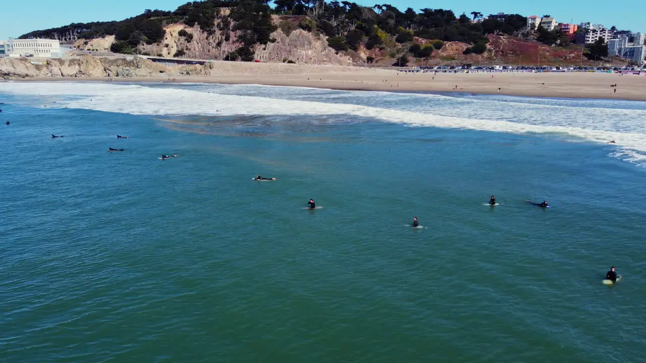 Surfers Lying and Sitting On Surfboard Floating In The Sea At Ocean Beach With Cliff House In San Francisco California